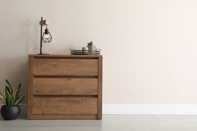Photo of Wooden chest of drawers with houseplants and lamp near beige wall. Space for text