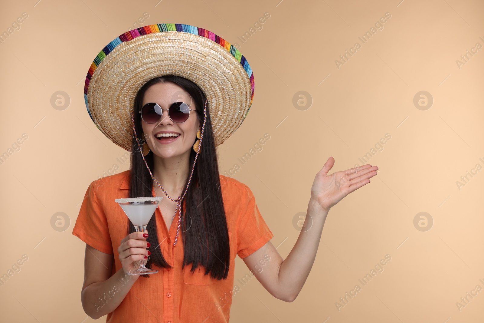 Photo of Young woman in Mexican sombrero hat with cocktail on beige background