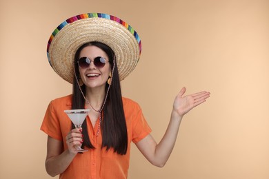 Young woman in Mexican sombrero hat with cocktail on beige background