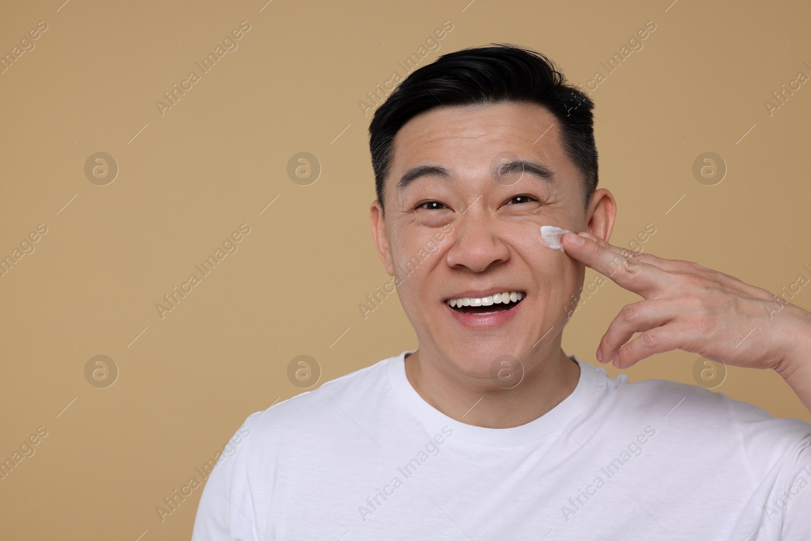 Photo of Handsome man applying cream onto his face on light brown background. Space for text