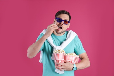 Man with 3D glasses eating tasty popcorn on color background