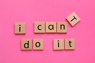 Photo of Motivation concept. Changing phrase from I Can't Do It into I Can Do It by removing wooden square with letter T on pink background, top view