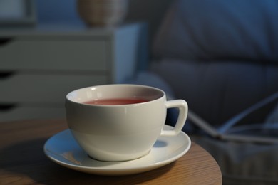 Cup of hot tea on wooden table at night