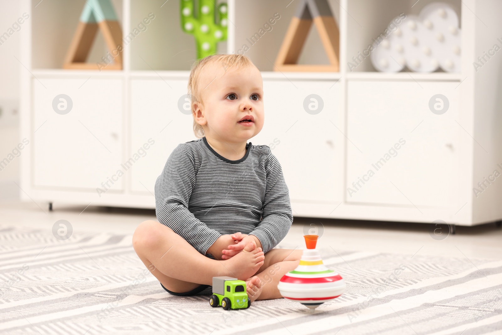 Photo of Children toys. Cute little boy with toy car and spinning top on rug at home