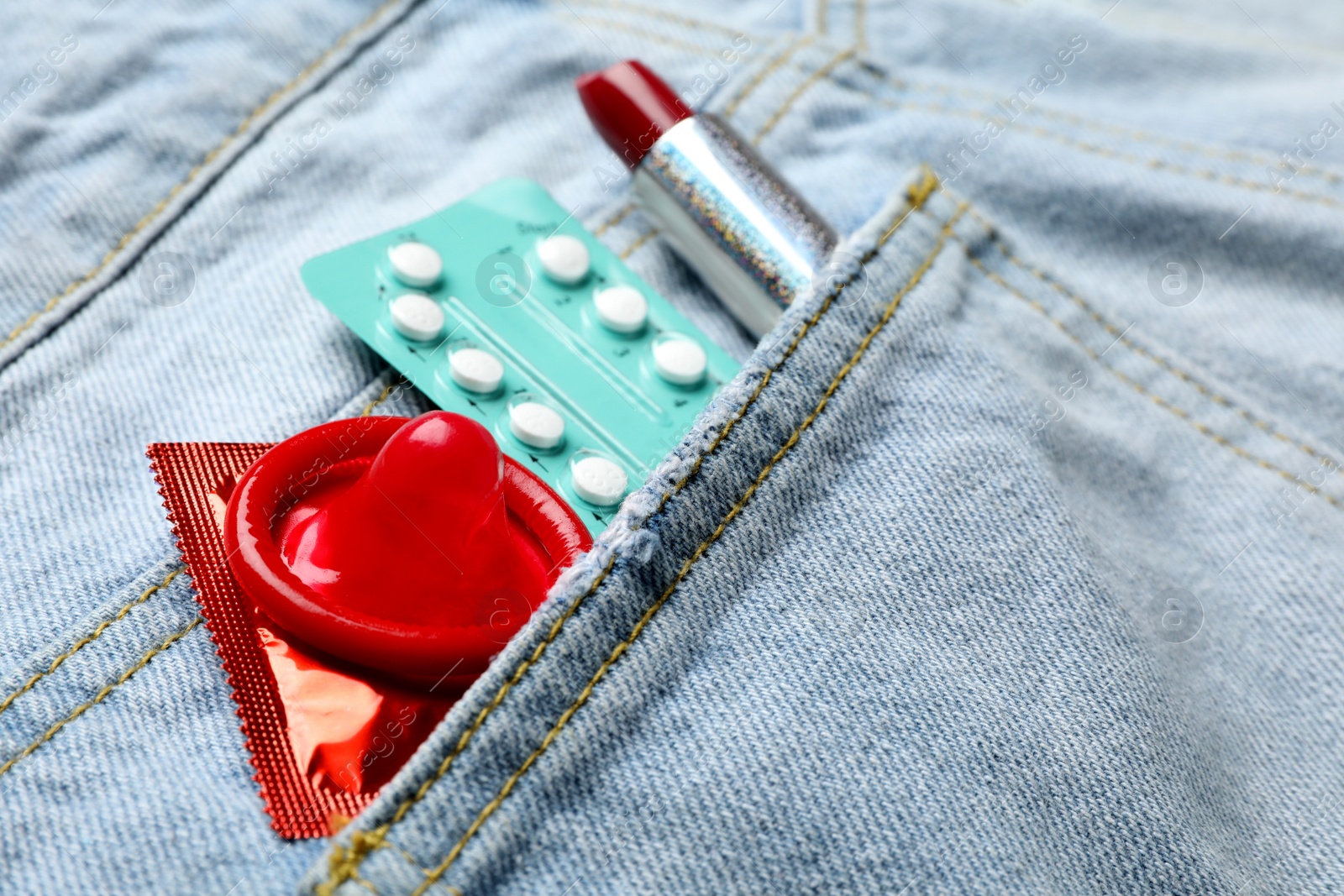 Photo of Red lipstick with condoms and birth control pills in pocket of jeans, closeup. Safe sex concept