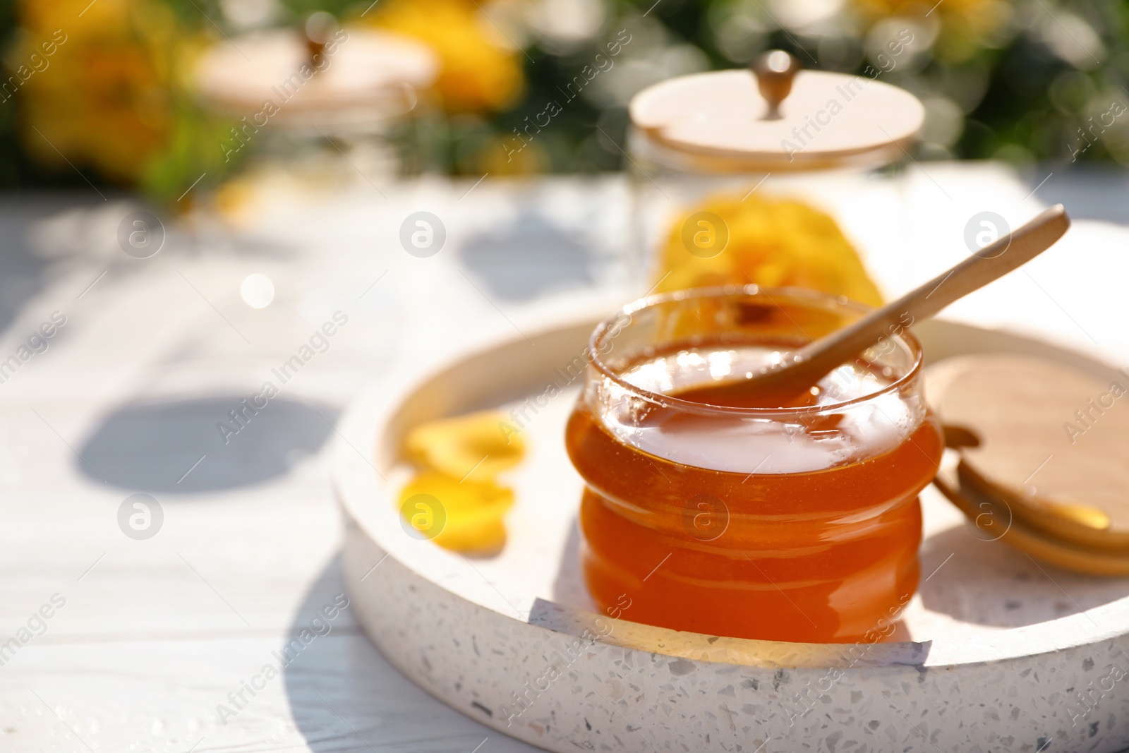 Photo of Jar with fresh rose honey on white wooden table outdoors. Space for text