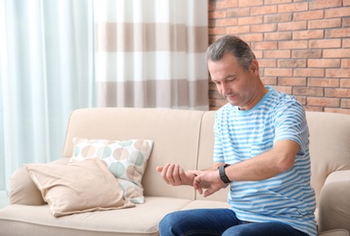 Photo of Mature man checking pulse with fingers in at home. Space for text