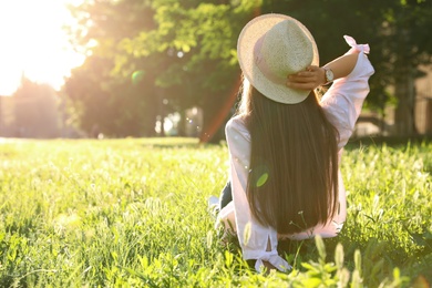 Photo of Young woman in straw hat sitting outdoors on sunny day, back view