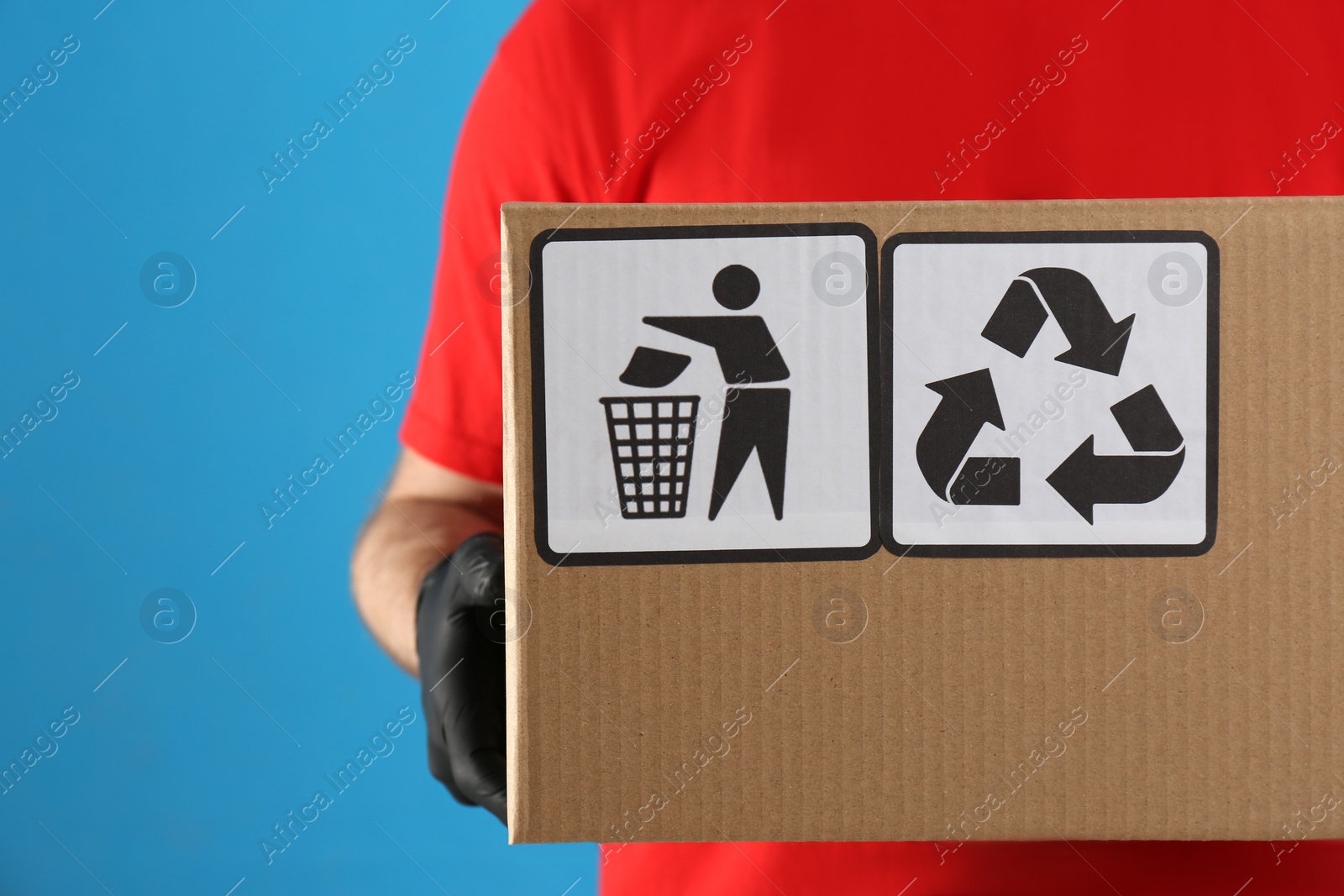 Photo of Courier holding cardboard box with different packaging symbols on blue background, closeup. Parcel delivery