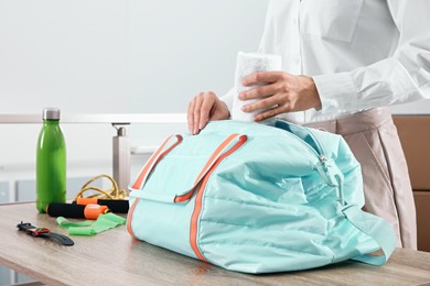 Photo of Businesswoman packing sports stuff for training into bag in office, closeup
