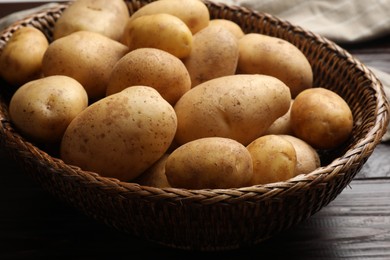 Photo of Raw fresh potatoes in wicker basket on wooden table, closeup