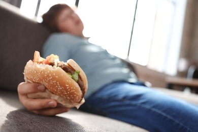 Photo of Overweight boy with burger sleeping on sofa at home