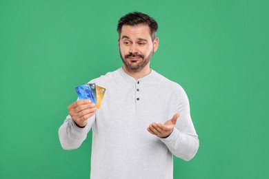 Confused man with credit cards on green background. Debt problem