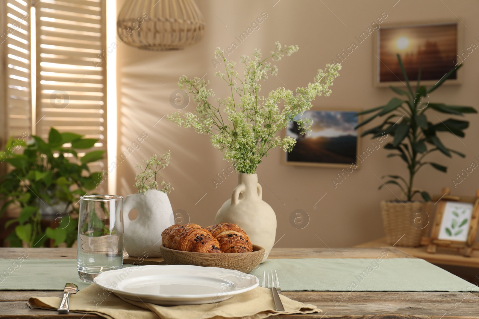 Photo of Clean tableware, flowers and fresh pastries on table in stylish dining room