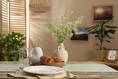 Photo of Clean tableware, flowers and fresh pastries on table in stylish dining room