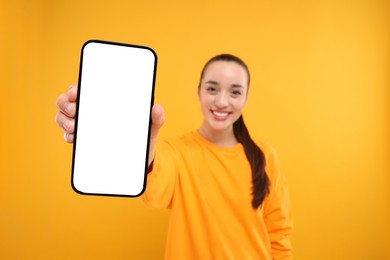 Photo of Young woman showing smartphone in hand on yellow background, selective focus. Mockup for design