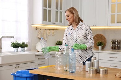 Smiling woman separating garbage at table in kitchen