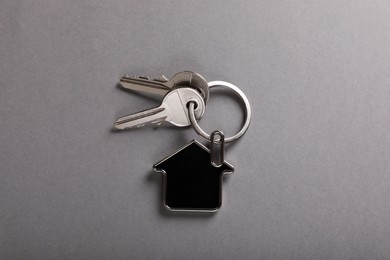 Keys with trinket in shape of house on grey background, top view. Real estate agent services