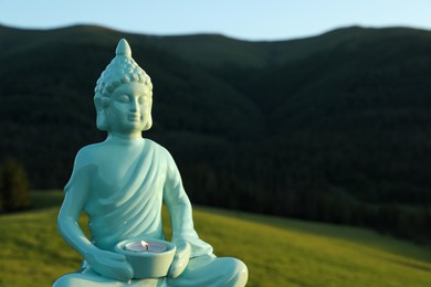 Photo of Decorative Buddha statue with burning candle in mountains, closeup. Space for text