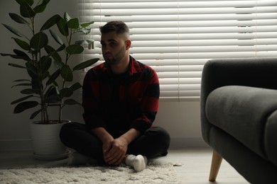 Sad man sitting near closed blinds indoors