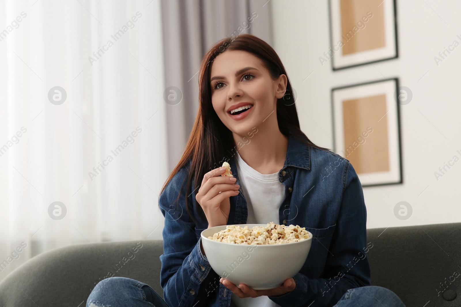 Photo of Beautiful woman with bowl of popcorn watching TV at home