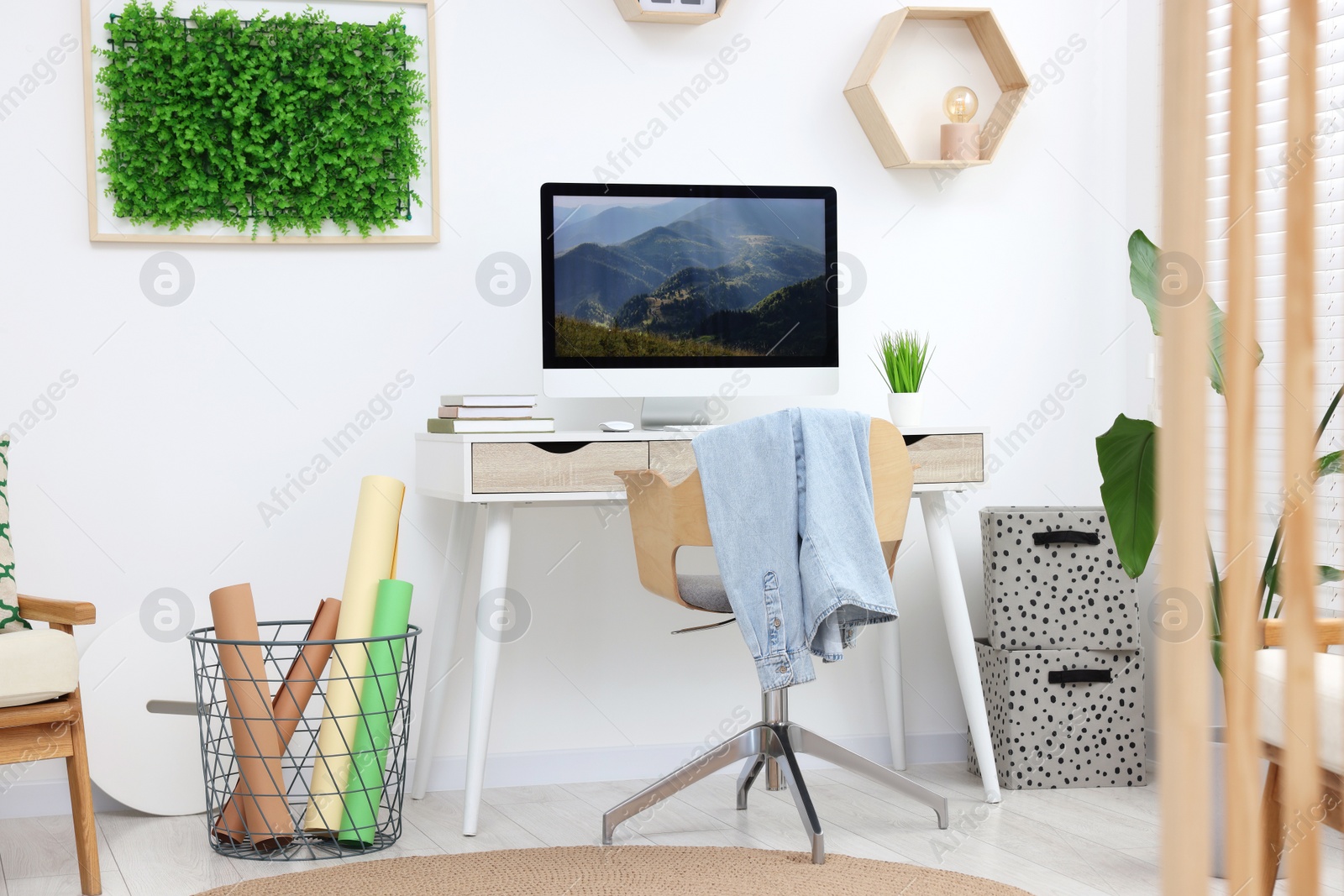 Photo of Green artificial plant wall panel and desk with computer in light room. Interior design