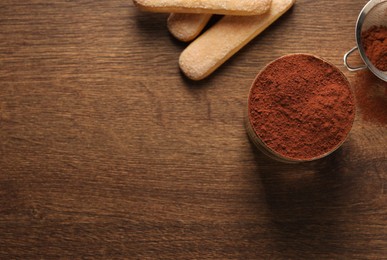 Photo of Delicious tiramisu in glass, biscuits and cocoa powder on wooden table, flat lay. Space for text