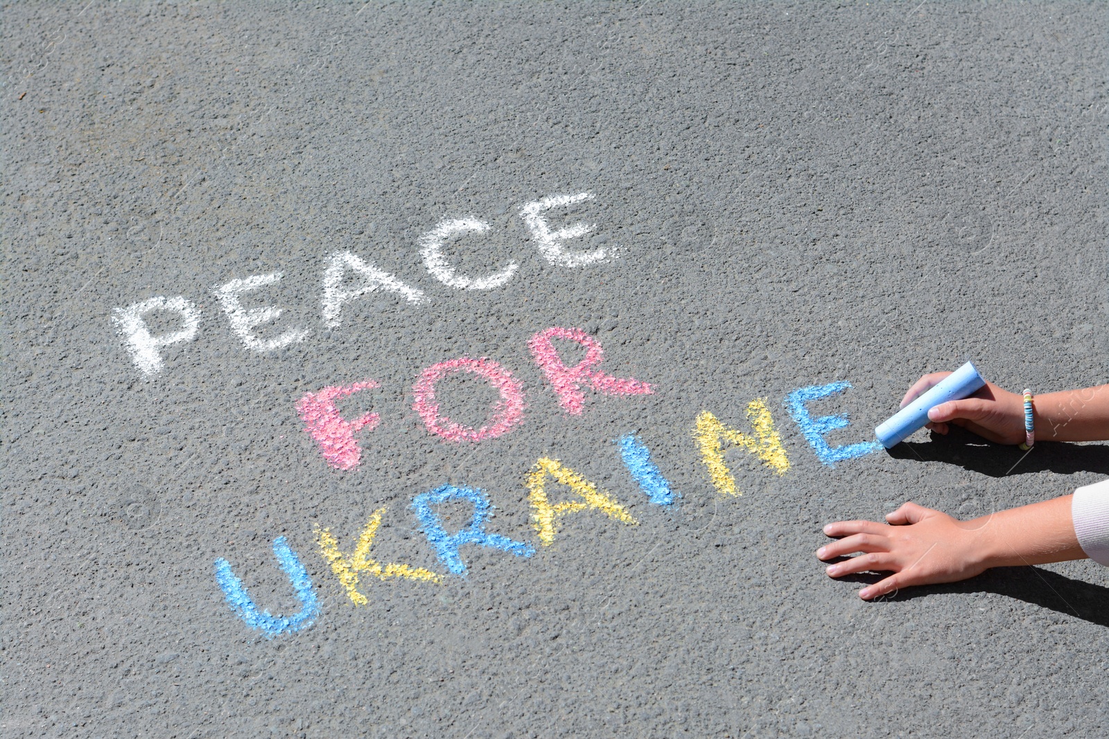 Photo of Girl writing Peace For Ukraine with colorful chalks on asphalt outdoors, closeup