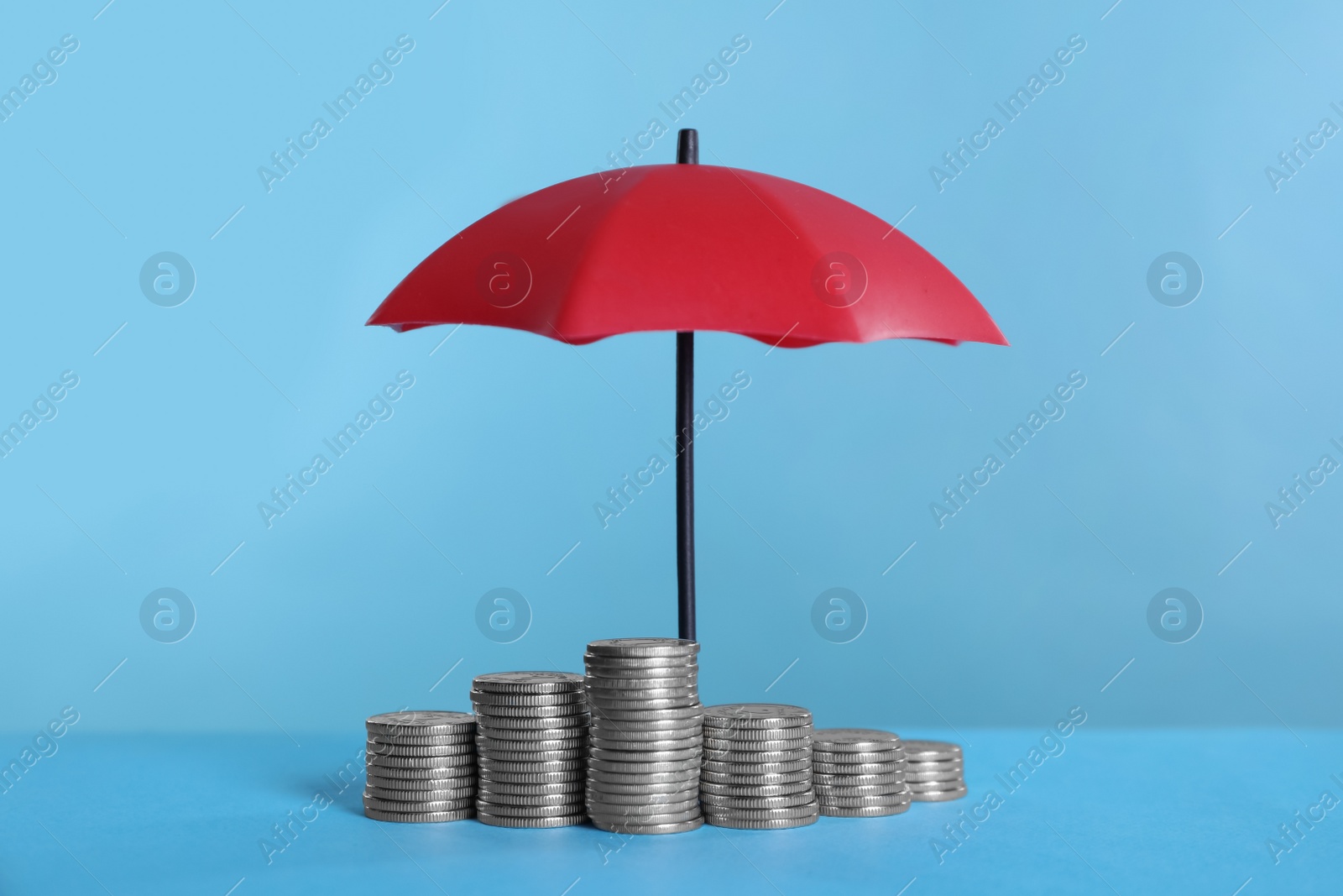 Photo of Small umbrella and coins on light blue background