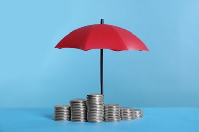 Photo of Small umbrella and coins on light blue background