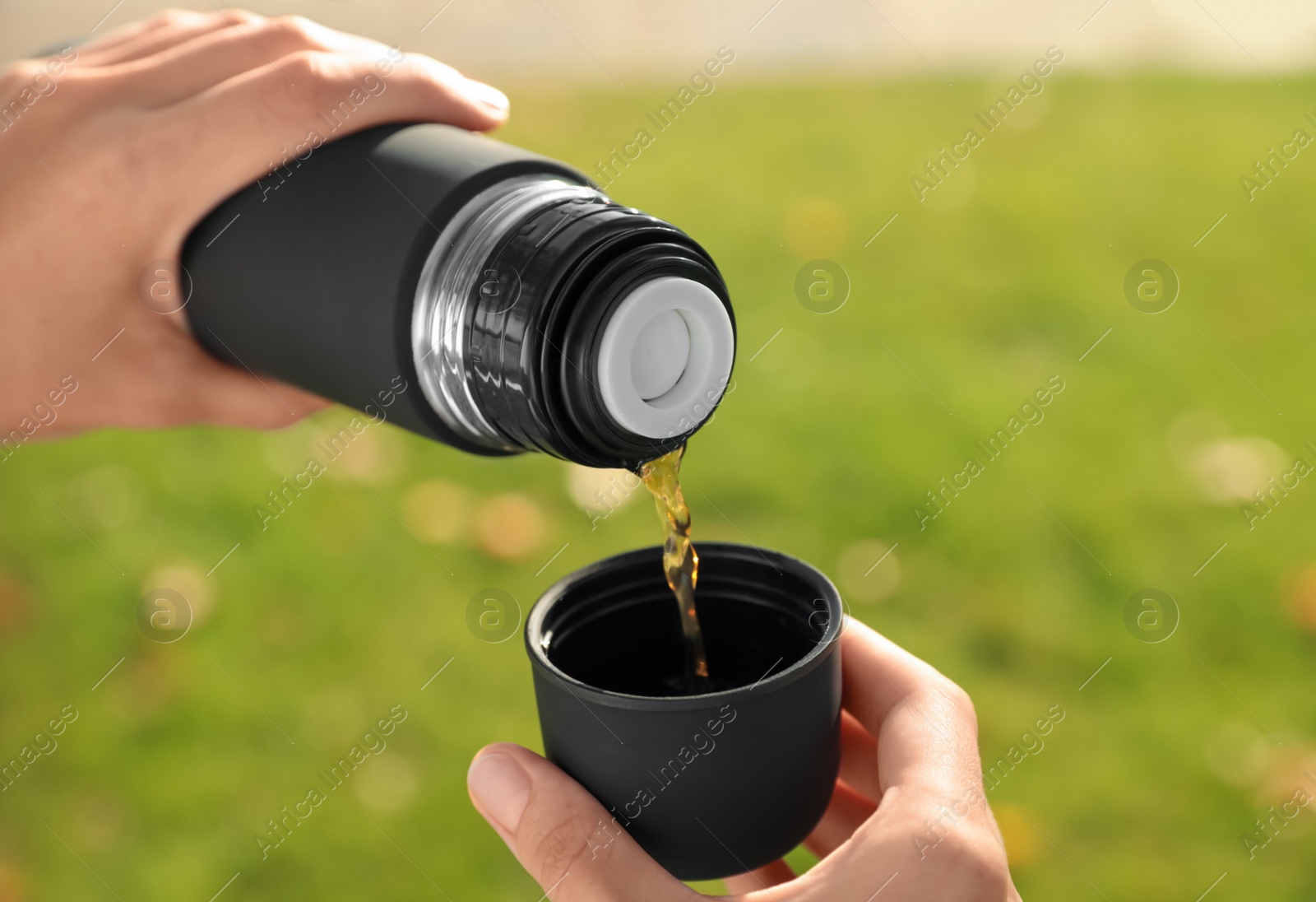 Photo of Woman pouring hot drink from thermos into cap outdoors, closeup