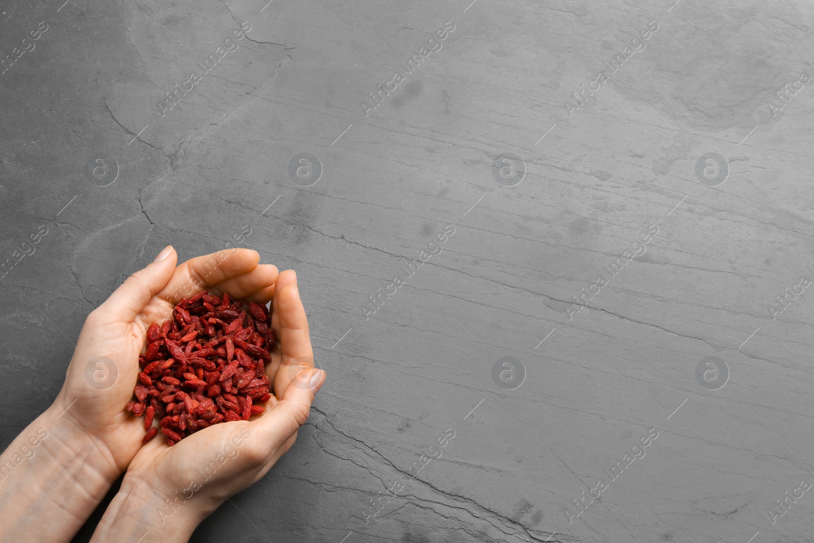 Photo of Woman holding red dried goji berries on grey stone background, top view. Space for text