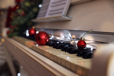 Red baubles and fairy lights on piano keys indoors, space for text. Christmas music