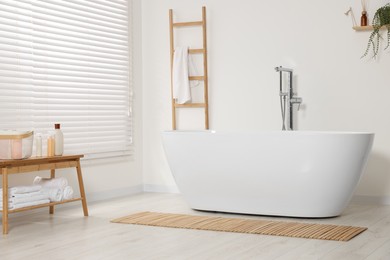 Photo of Stylish bathroom interior with ceramic tub, care products and terry towels on table