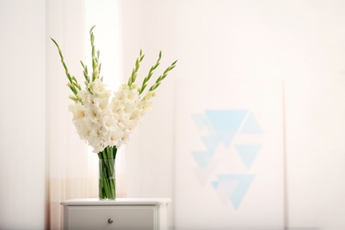 Vase with beautiful white gladiolus flowers on drawer chest in room, space for text