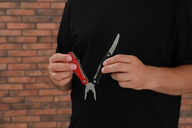 Photo of Man holding multitool near brick wall, closeup