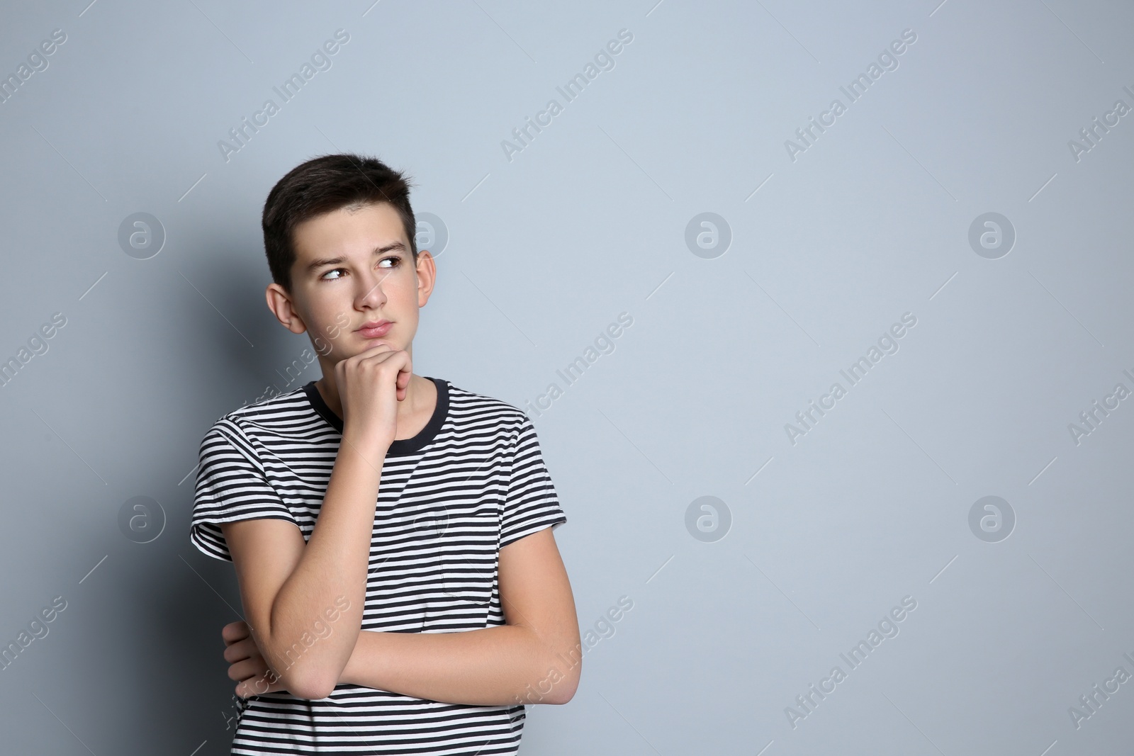 Photo of Thoughtful teenage boy on grey background. Space for text