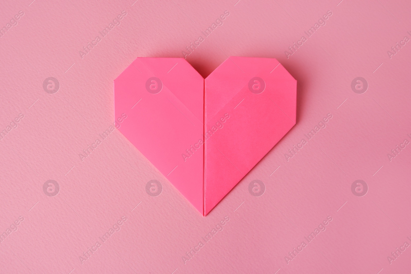 Photo of Origami art. Paper heart on pink background, top view