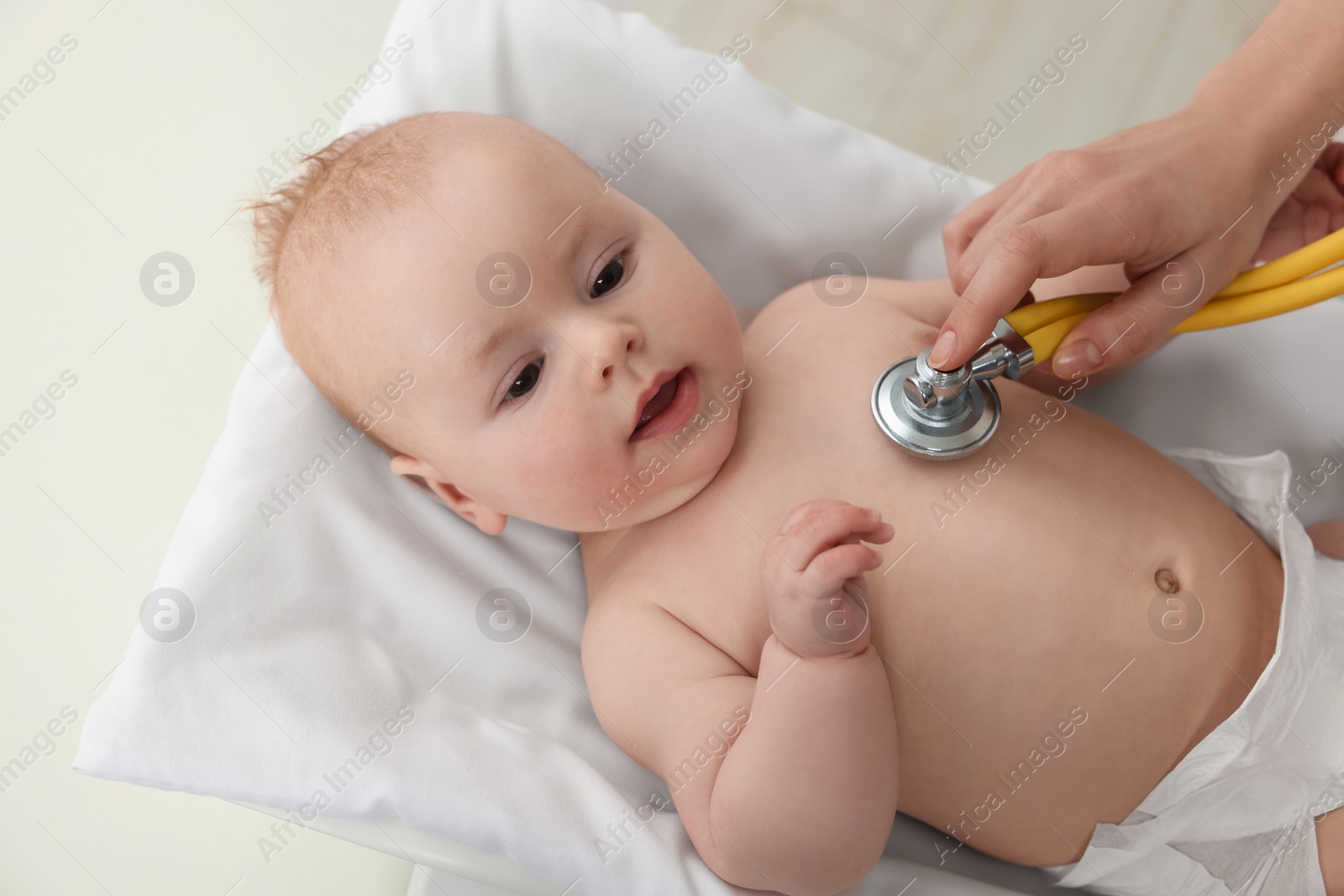 Photo of Pediatrician examining cute little baby with stethoscope in clinic, closeup