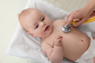 Pediatrician examining cute little baby with stethoscope in clinic, closeup