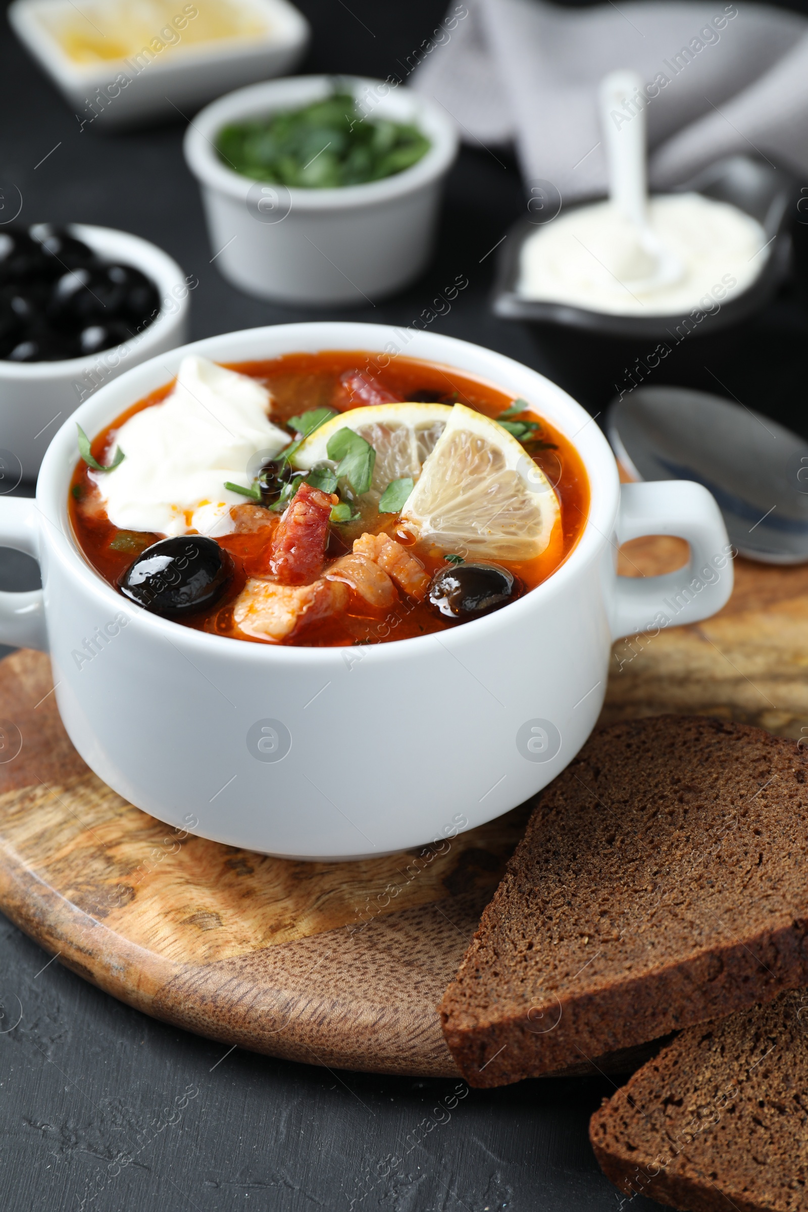 Photo of Meat solyanka soup with sausages, olives and vegetables in bowl served on grey textured table, closeup