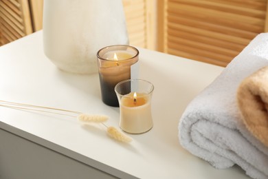 Photo of Candles and stacked towels on chest of drawers. Interior design