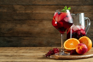 Photo of Glass and jug of Red Sangria with fruits on wooden table, space for text