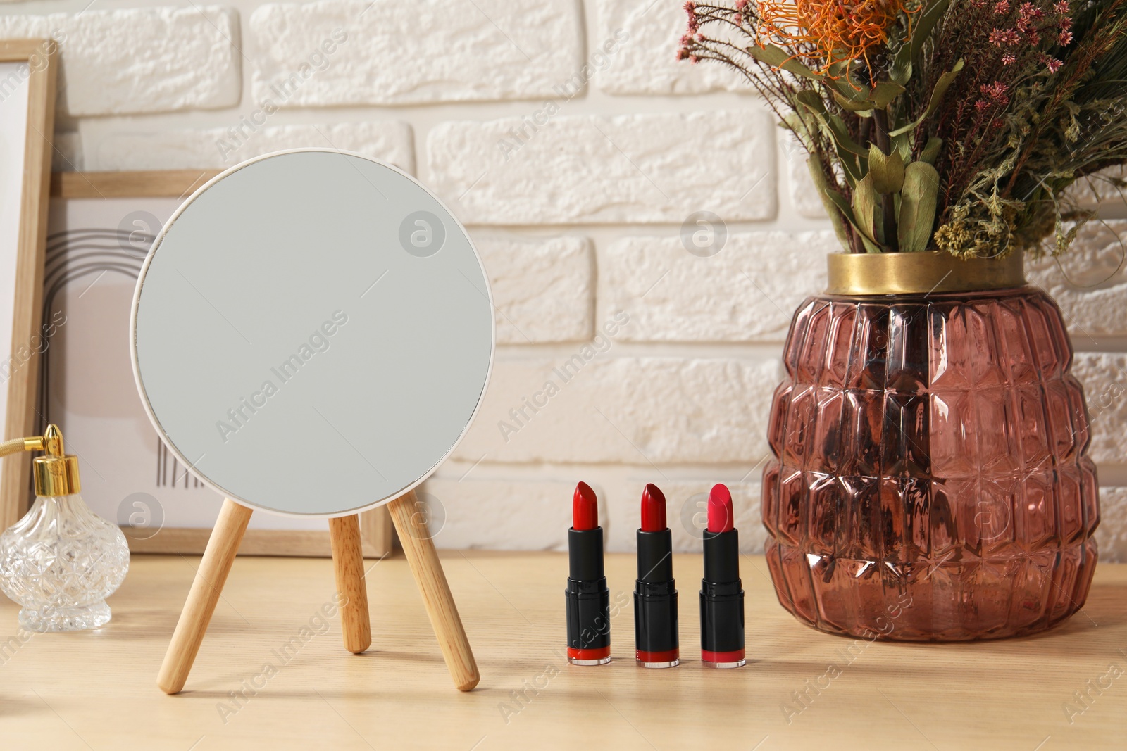 Photo of Mirror, makeup products, perfume and vase on wooden dressing table