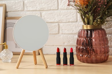 Mirror, makeup products, perfume and vase on wooden dressing table