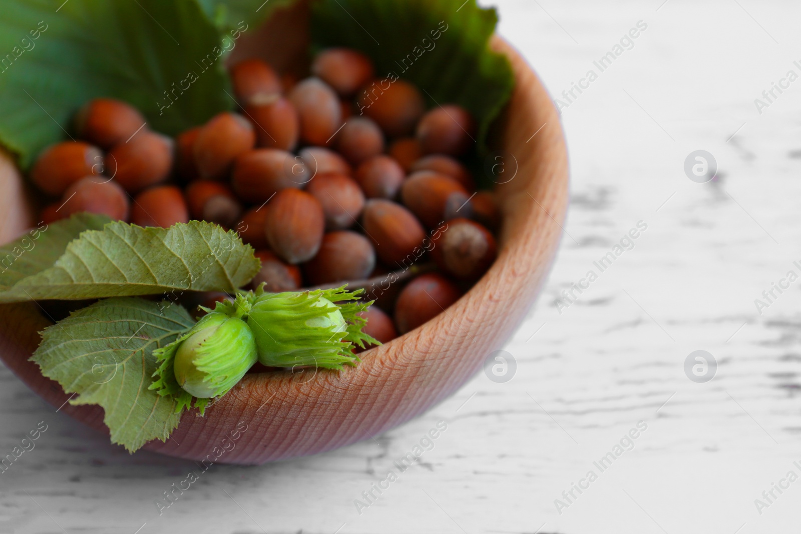 Photo of Bowl with hazelnuts and leaves on white wooden table, closeup