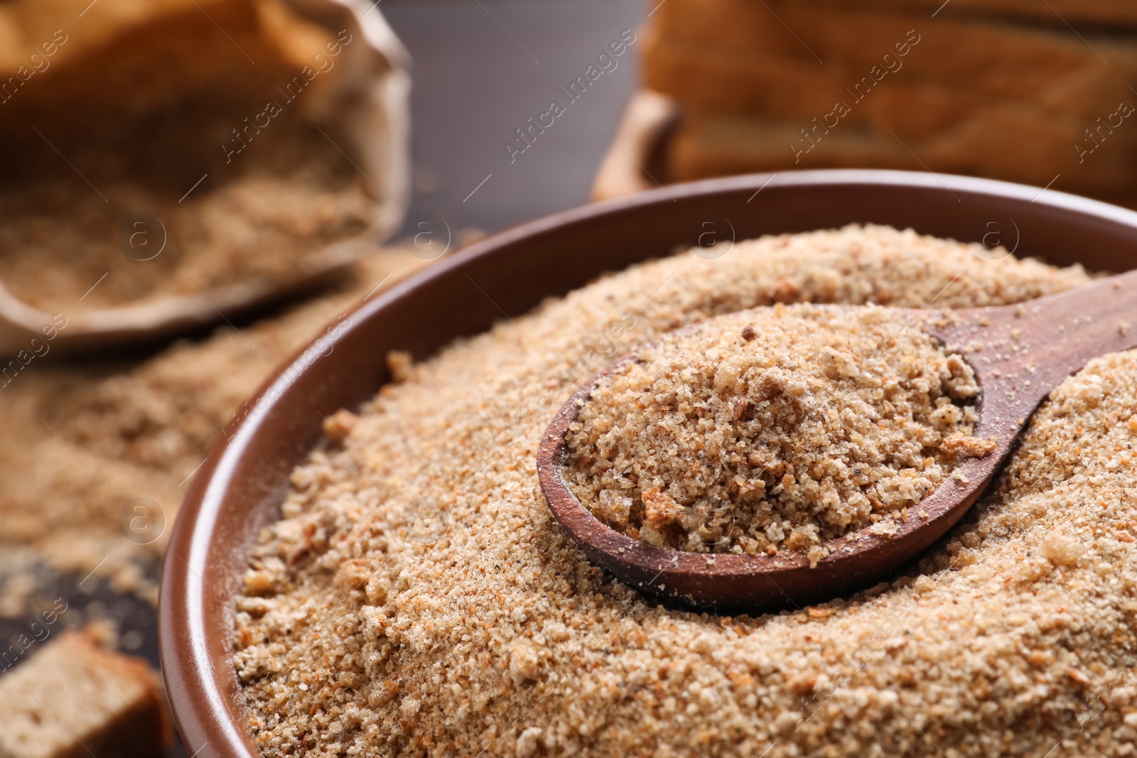 Photo of Fresh breadcrumbs in bowl and spoon on table, closeup