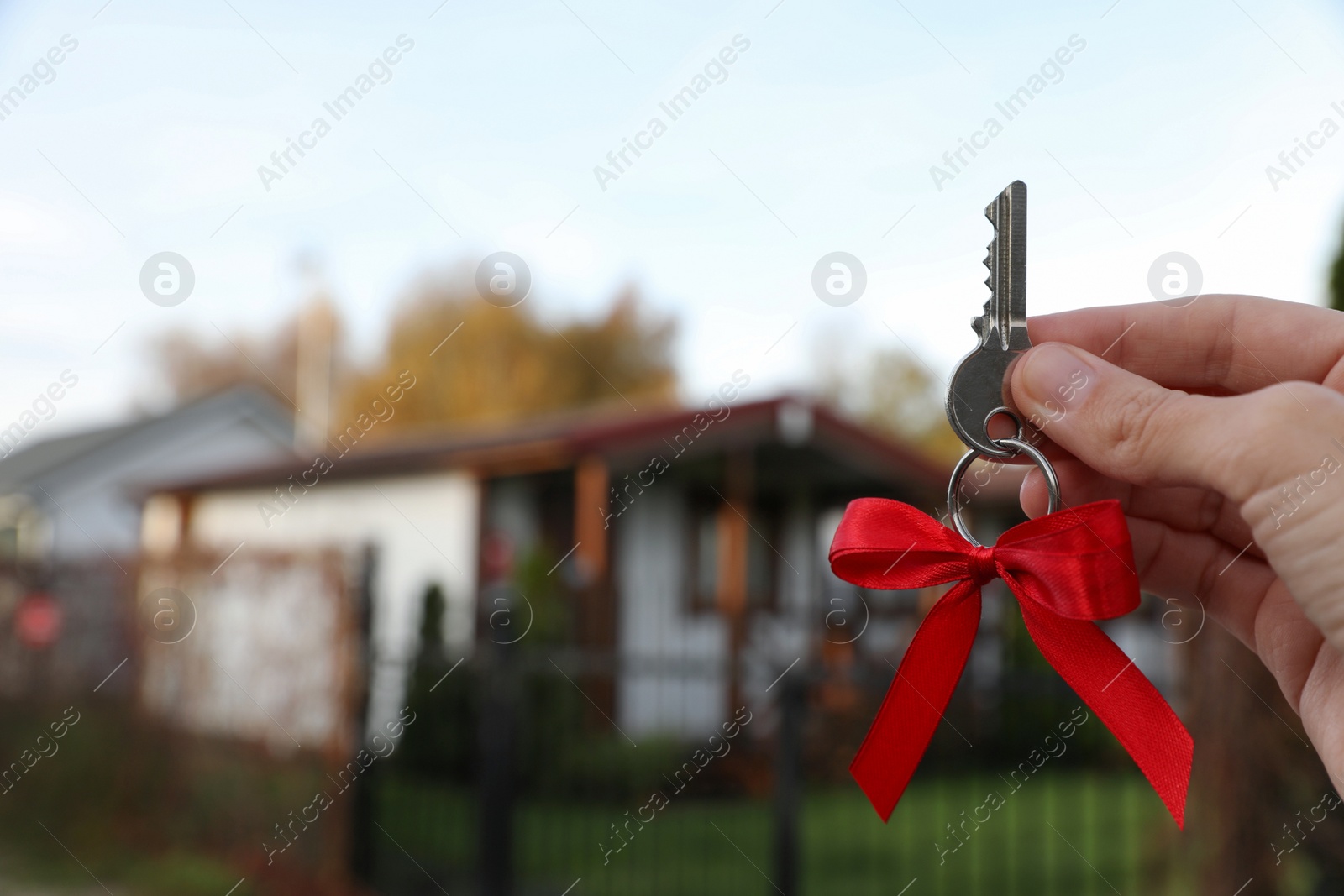 Photo of Woman holding key with bow near house outdoors, closeup. Space for text