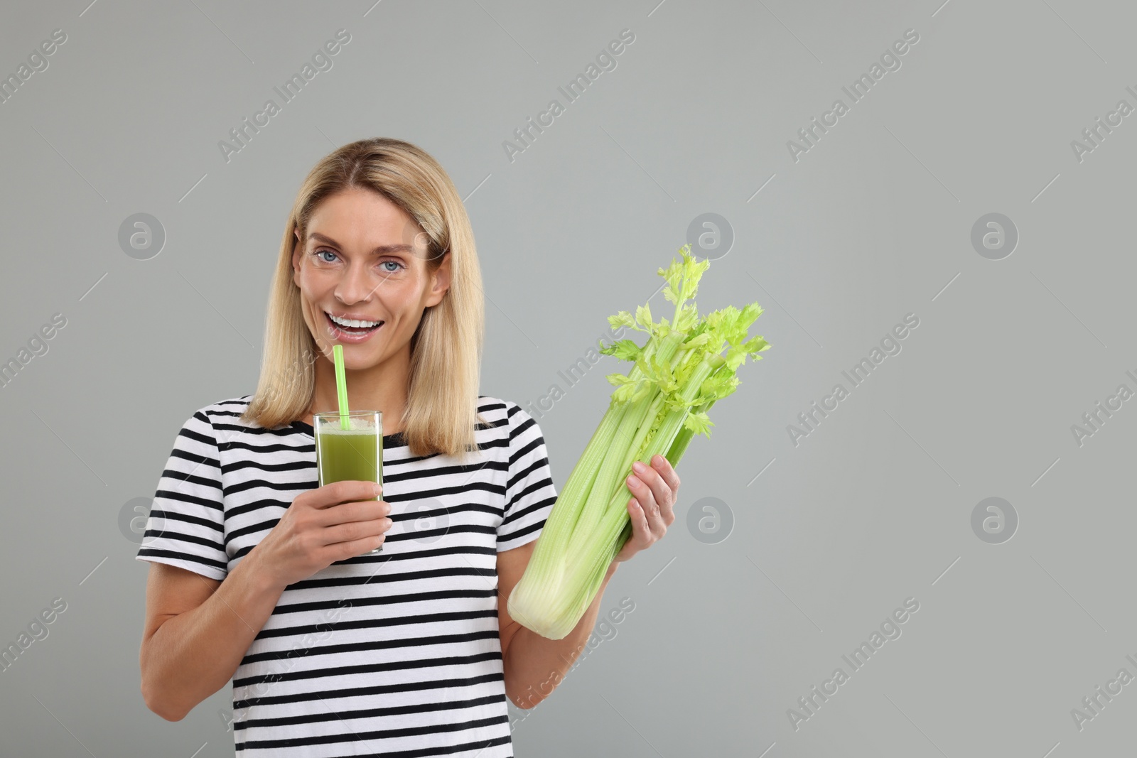 Photo of Happy woman holding glass with tasty celery juice and fresh vegetable on light grey background. Space for text