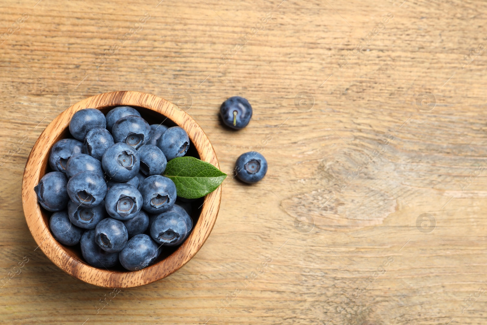 Photo of Bowl of fresh tasty blueberries on wooden table, flat lay. Space for text